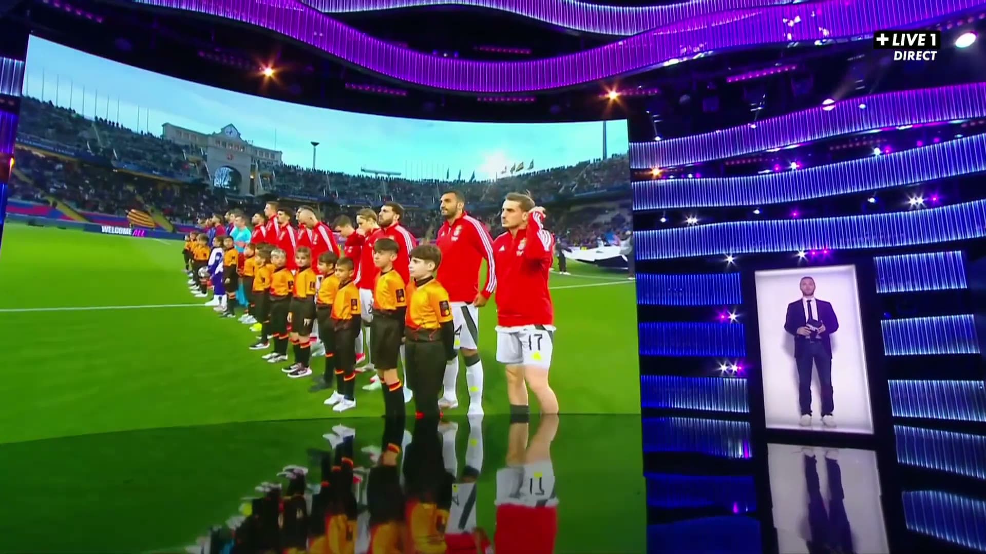 A journalist appearing as a life-size hologram in a Holobox in the CANAL+ studio, beside a stadium LED wall.